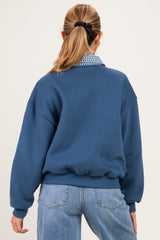 woman wearing a blue maternity sweatshirt with a relaxed fit and layered collar, featuring a gingham print underneath
