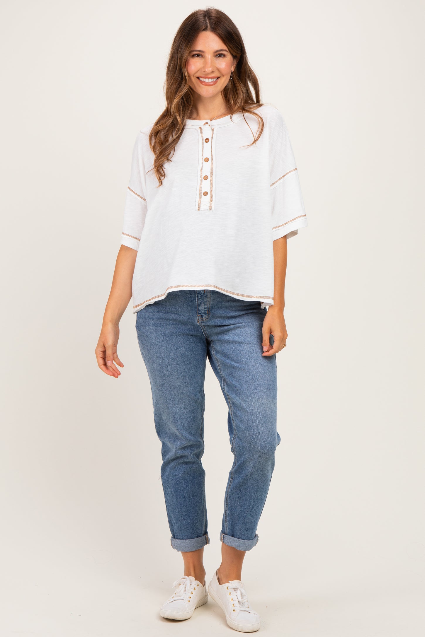 woman wearing a white maternity top with button details and rolled sleeves paired with light blue jeans