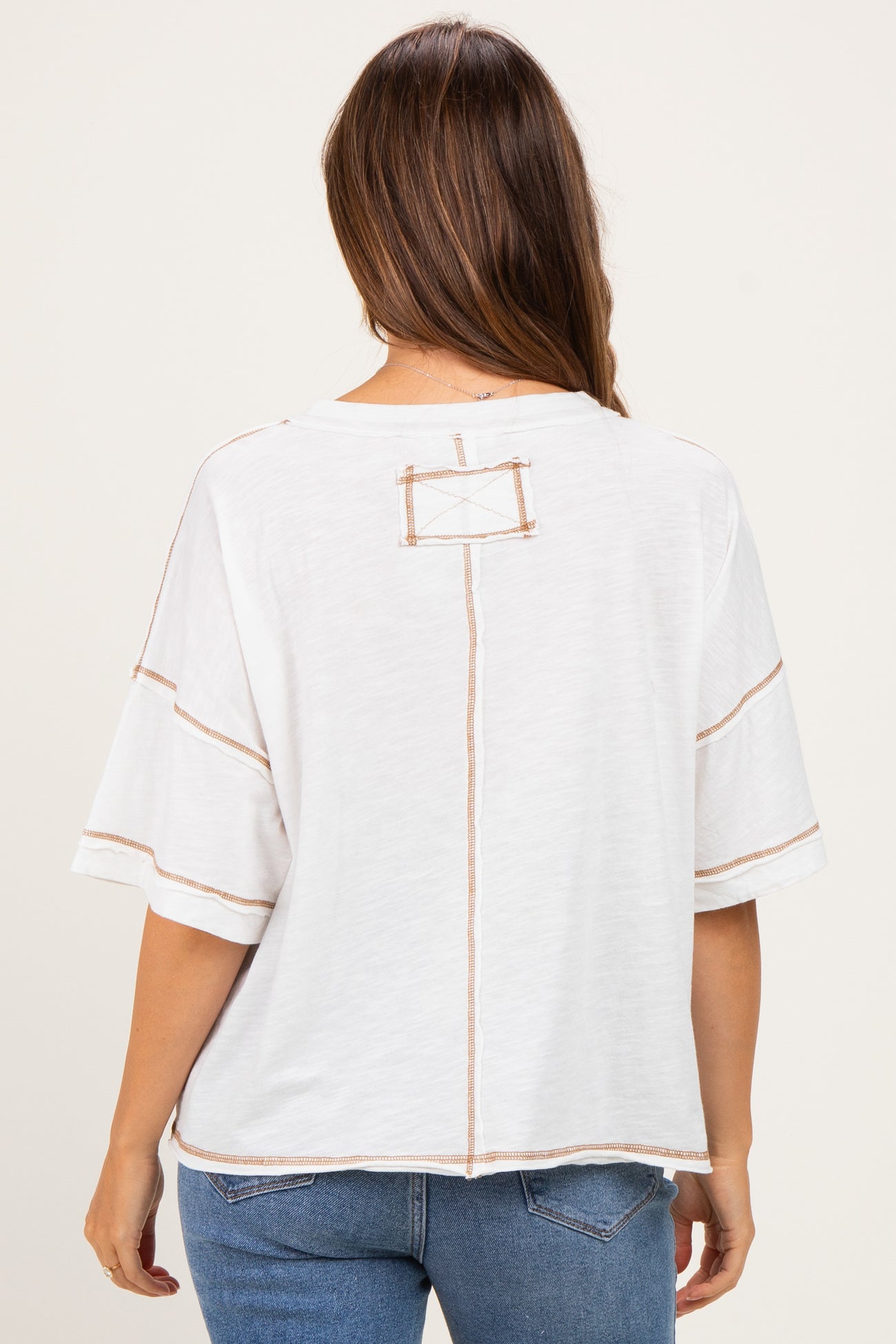 woman wearing a white maternity top with contrast stitching and a relaxed fit, seen from the back