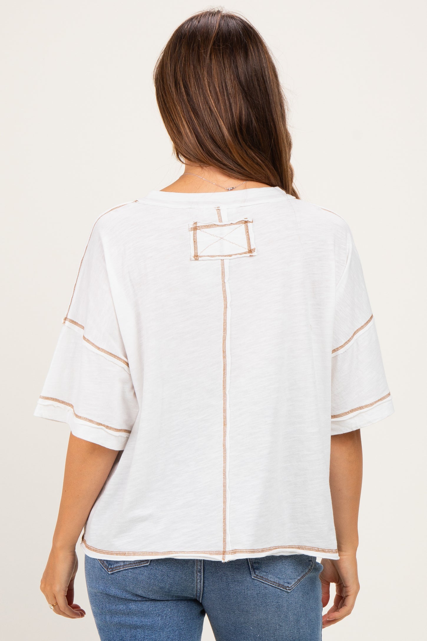 woman wearing a white maternity top with contrast stitching and a relaxed fit, seen from the back