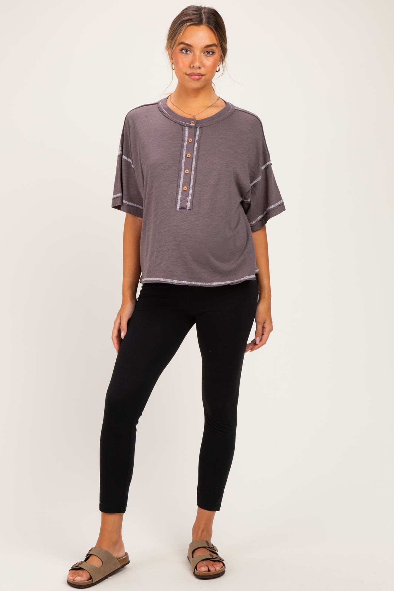woman wearing a dark gray short sleeve maternity top with buttons and black maternity leggings
