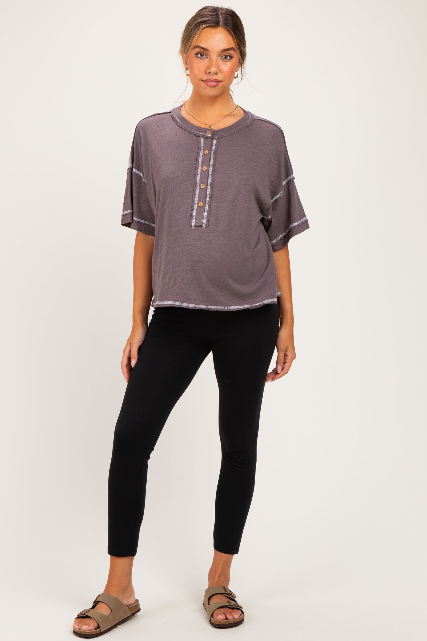 woman wearing a dark gray short sleeve maternity top with buttons and black maternity leggings