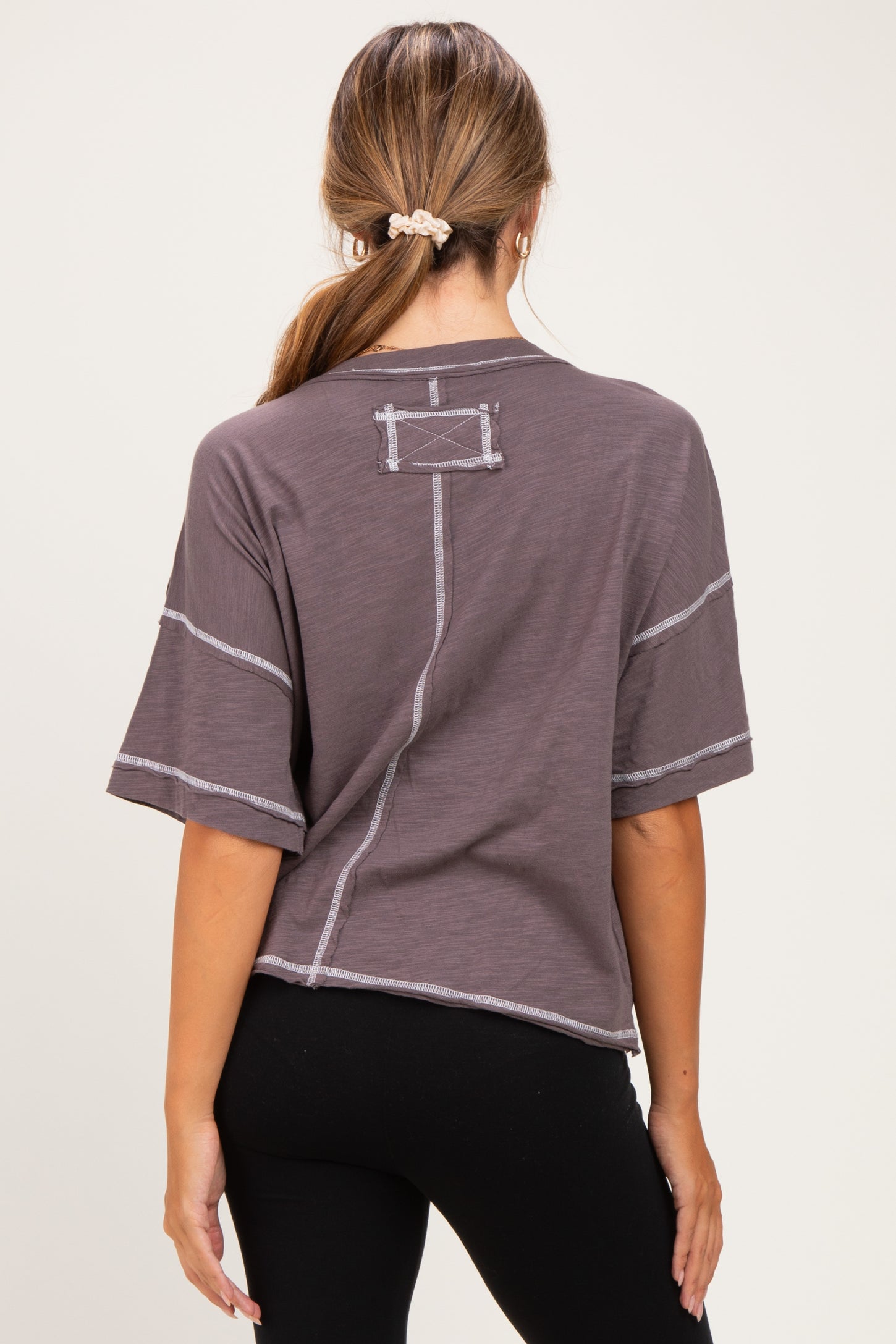 woman wearing a loose-fitting dark gray maternity top with short sleeves and contrasting stitching details