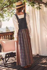 woman wearing a denim bib dress with a plaid maxi skirt, standing on a deck with a straw hat and a sunlit background