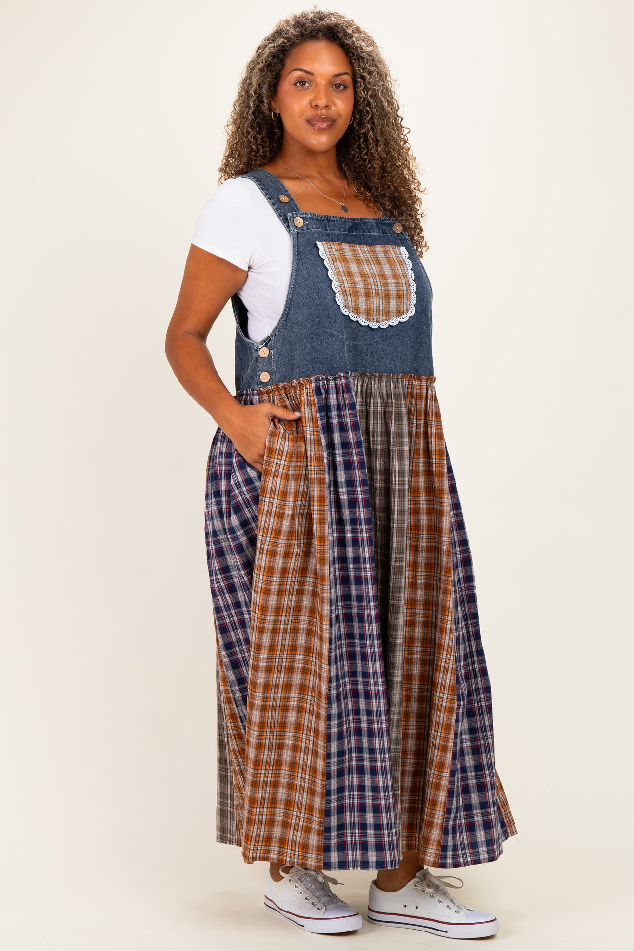 woman wearing a blue denim maxi jumper dress with plaid skirt and pockets, styled with a white t-shirt underneath