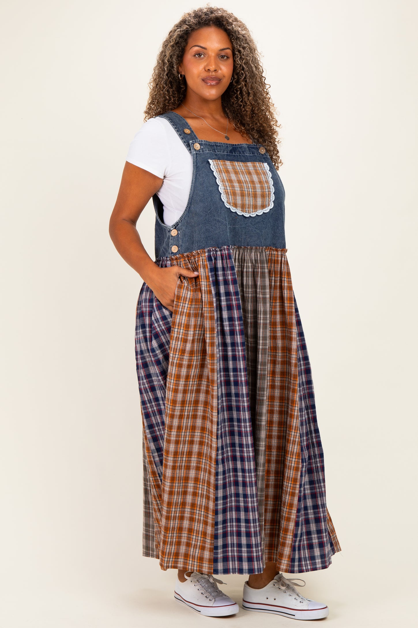 woman wearing a blue denim maxi jumper dress with plaid skirt and pockets, styled with a white t-shirt underneath