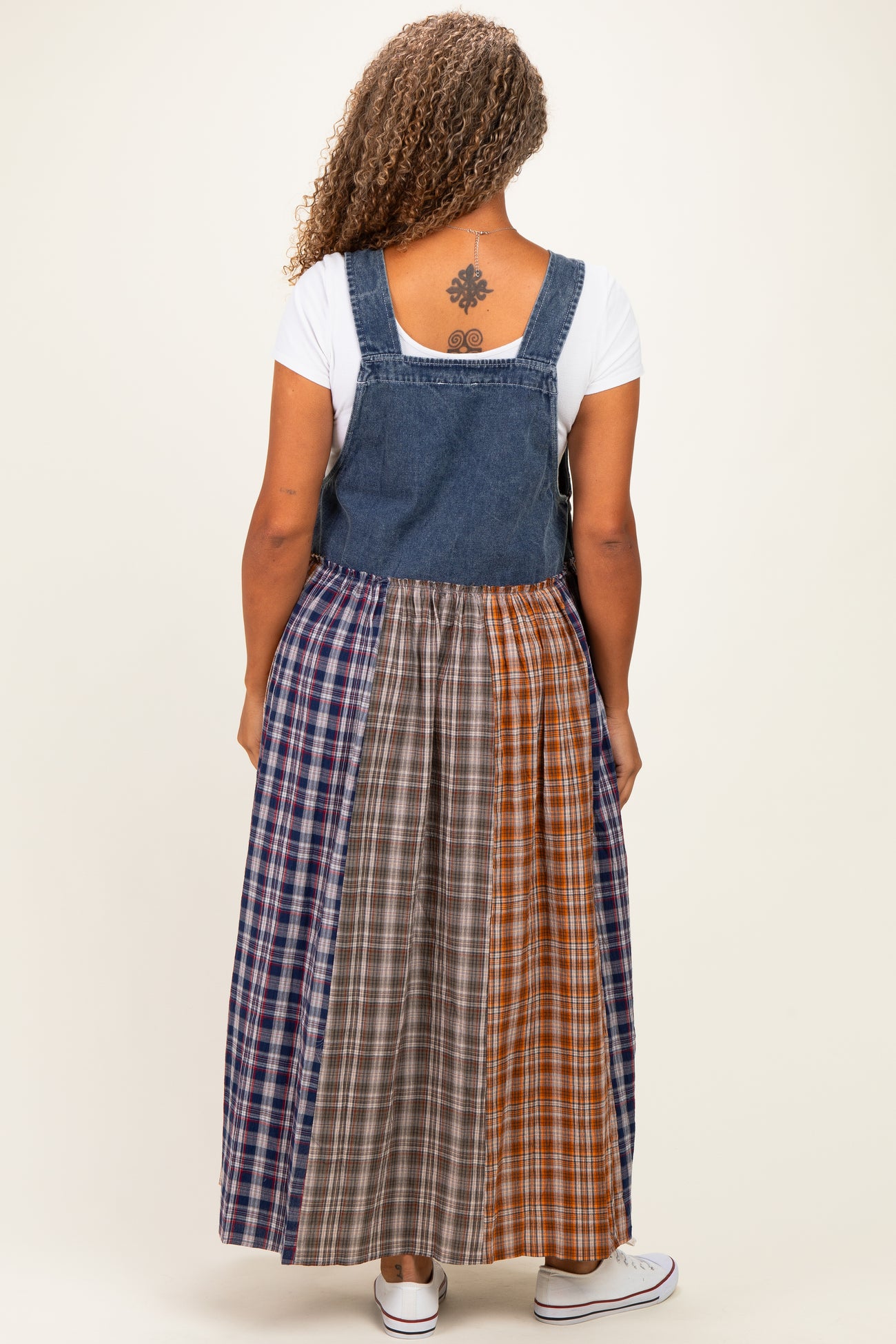 woman wearing a sleeveless denim jumper dress with a plaid multi-colored skirt and a white t-shirt underneath
