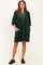 woman wearing a dark green corduroy tunic dress with a v-neck and pockets, styled with black slip-on shoes