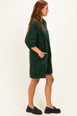 woman wearing a dark green corduroy dress with three-quarter sleeves and pockets, standing sideways