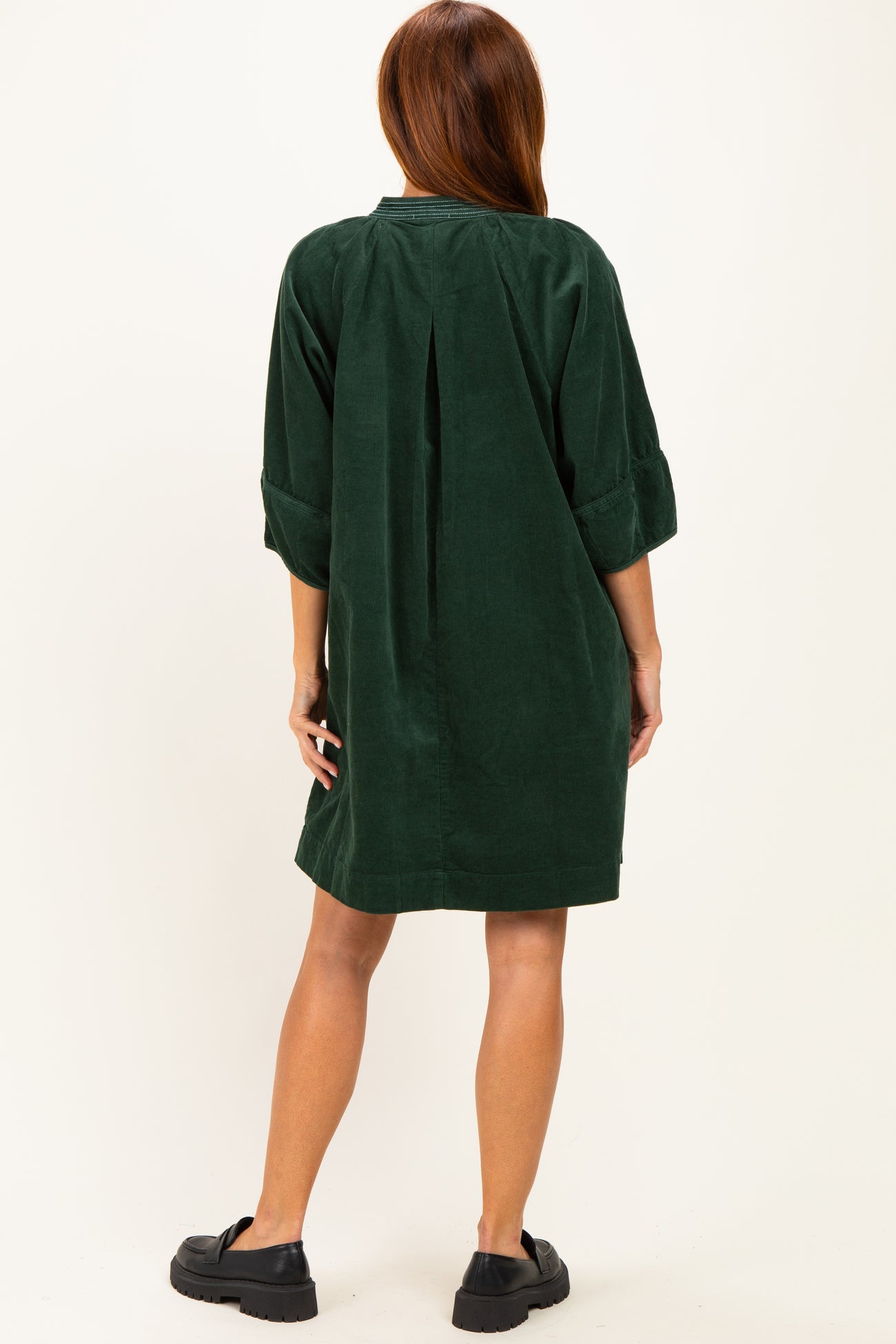 woman wearing a dark green corduroy shirt dress with three-quarter sleeves and a back pleat, styled with black clogs