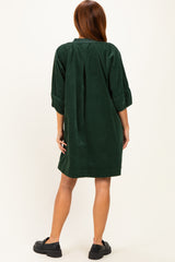 woman wearing a dark green corduroy shirt dress with three-quarter sleeves and a back pleat, styled with black clogs