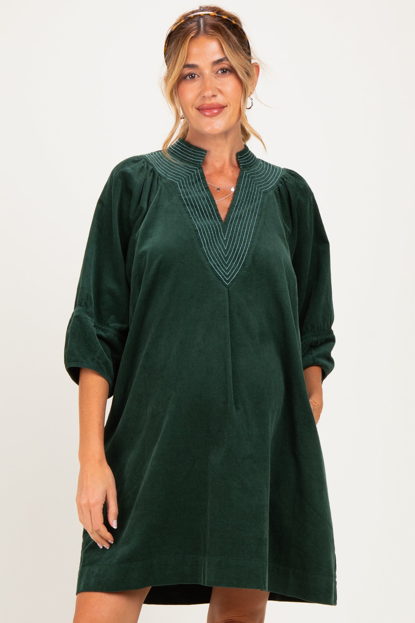 woman wearing a dark green maternity dress with a v-neck and three-quarter sleeves, featuring decorative stitching