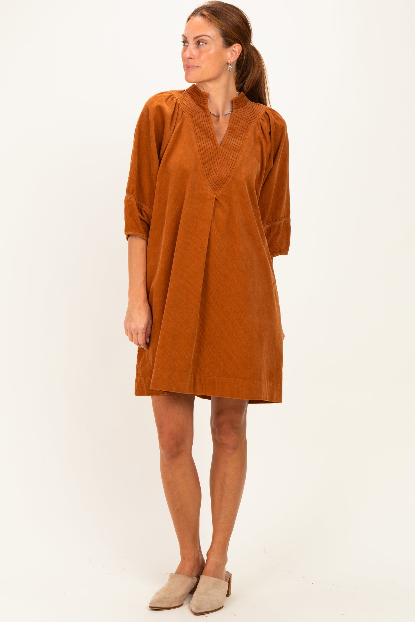 woman wearing an orange corduroy tunic dress with a v-neck and three-quarter sleeves, standing in a relaxed pose