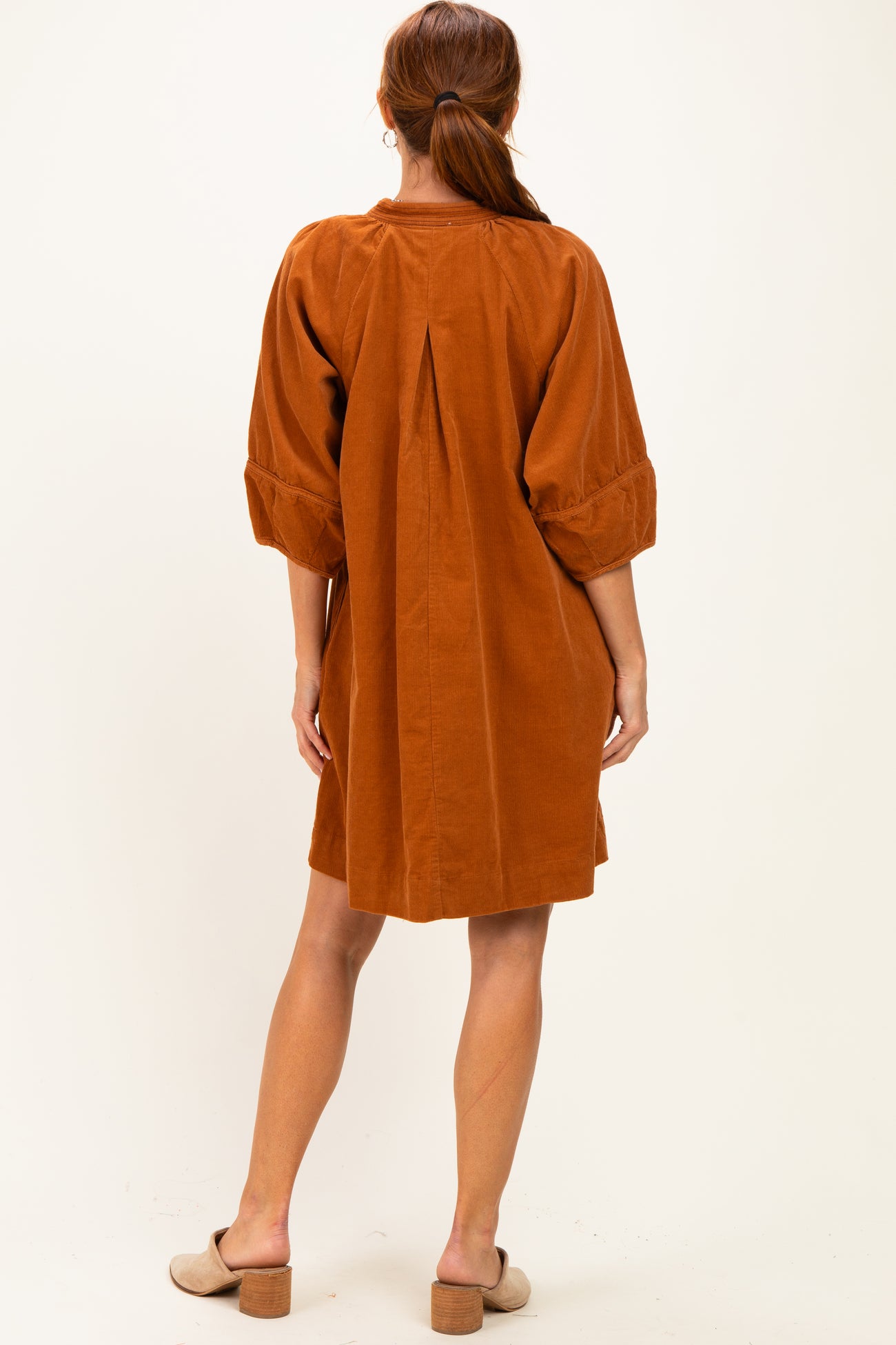 woman wearing an orange corduroy dress with balloon sleeves and a back pleat, showing the back view