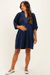 woman wearing a navy blue maternity dress with a v-neck and pleated detail, holding her baby bump