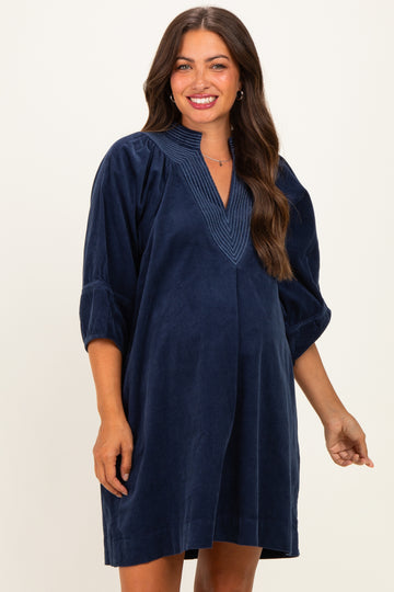 woman wearing a navy blue corduroy maternity dress with a v-neck and puff sleeves