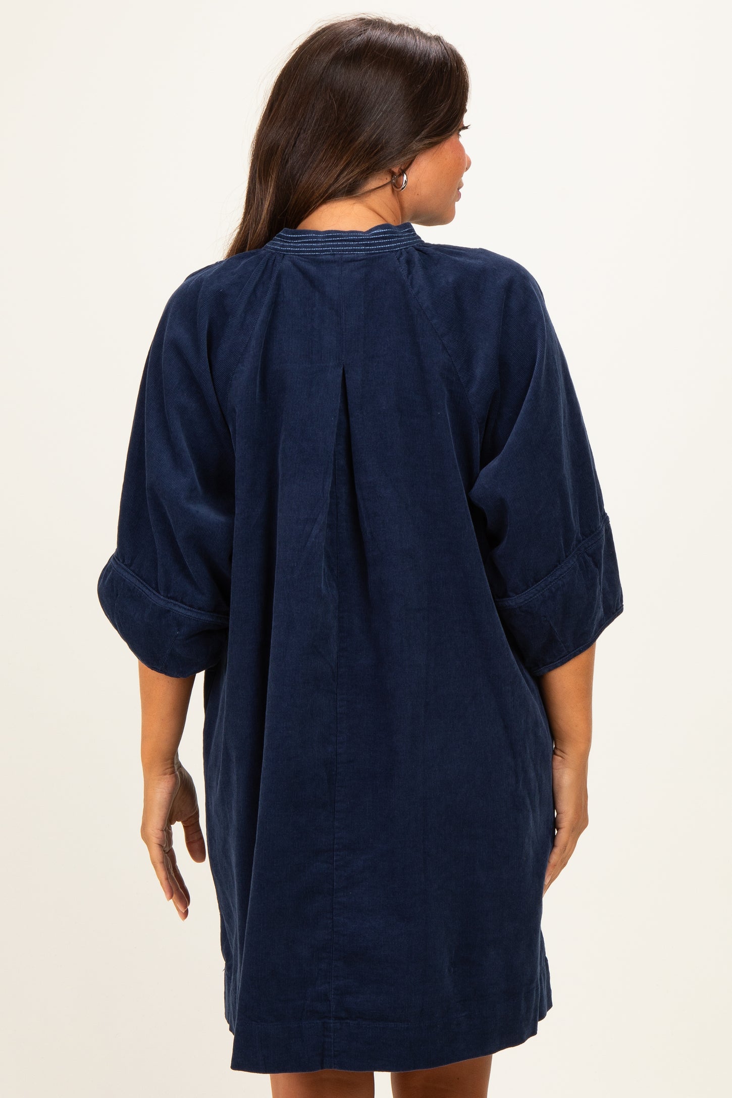 woman wearing a navy blue maternity dress with 3/4 sleeves and back pleat detail, showing her baby bump