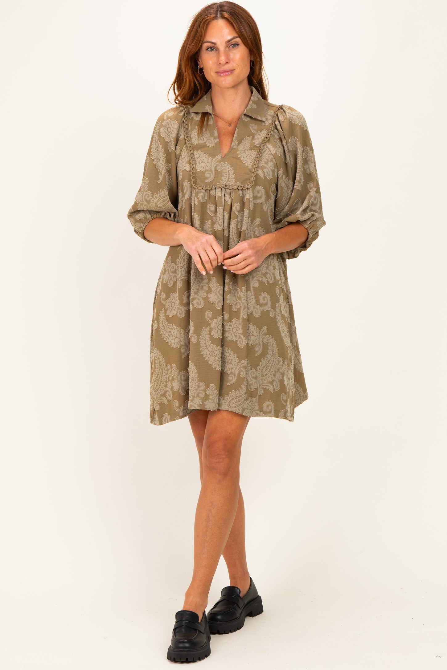 woman wearing a tan paisley print short-sleeve dress with a collared neckline and a loose fit
