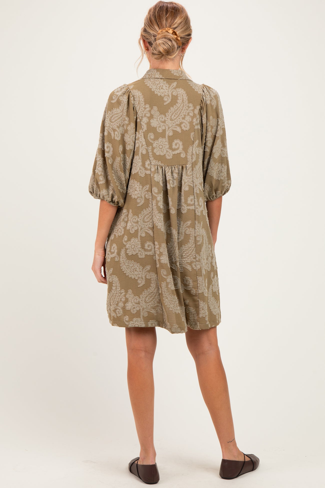woman wearing an olive green maternity dress with a floral pattern and puff sleeves, showing the back view