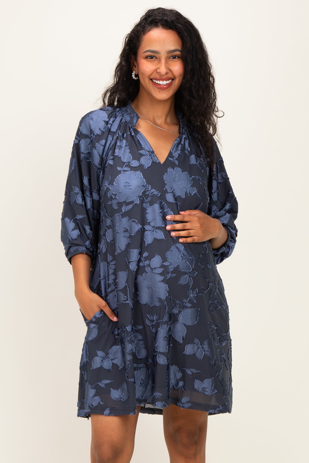 woman wearing a navy floral maternity dress with a v-neck and pockets, gently cradling her baby bump