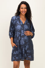 woman wearing a navy floral maternity dress with a v-neck and pockets, gently cradling her baby bump
