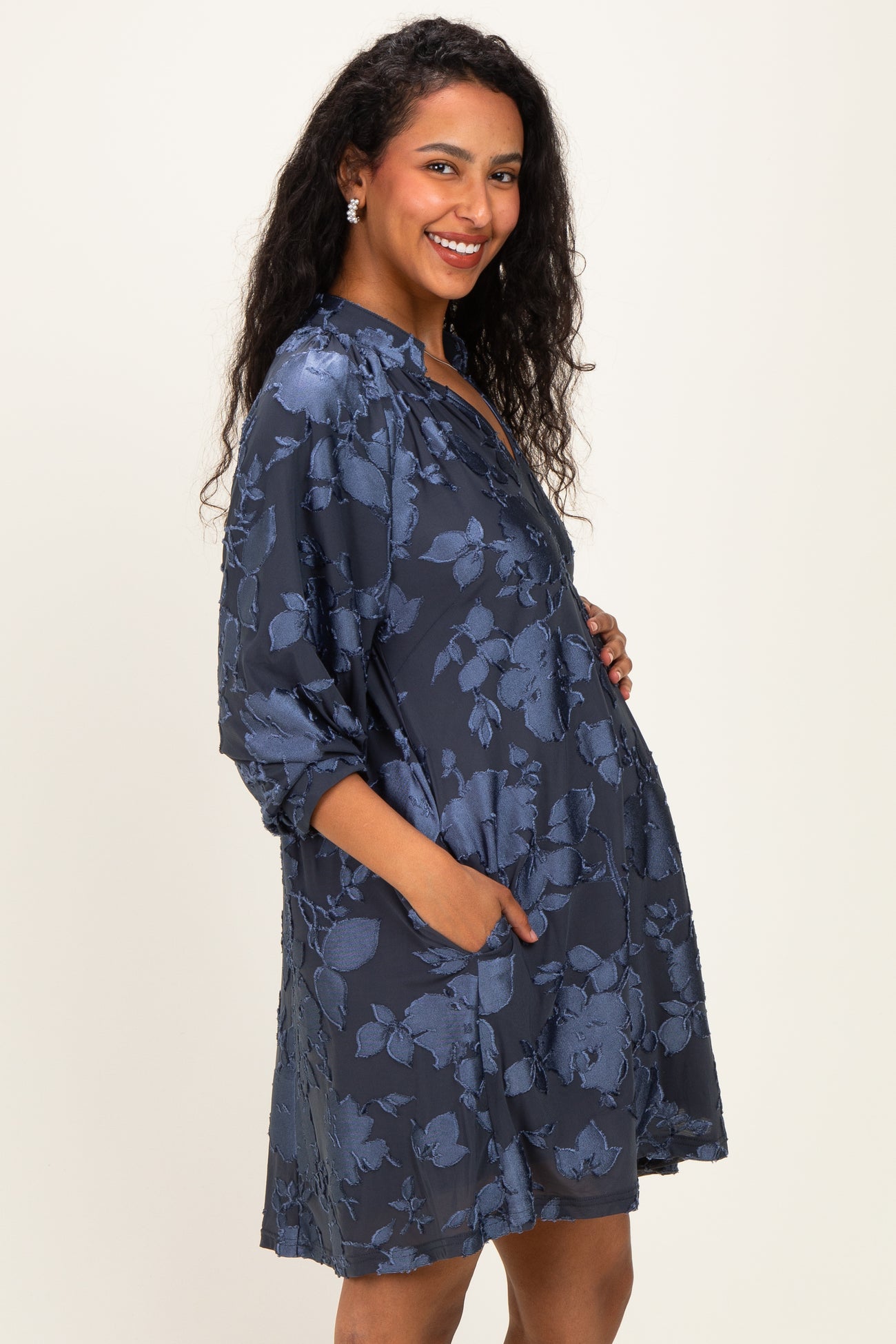 woman wearing a dark blue floral maternity dress with pockets and a baby bump visible