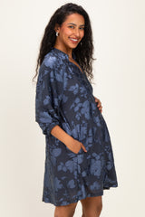 woman wearing a dark blue floral maternity dress with pockets and a baby bump visible