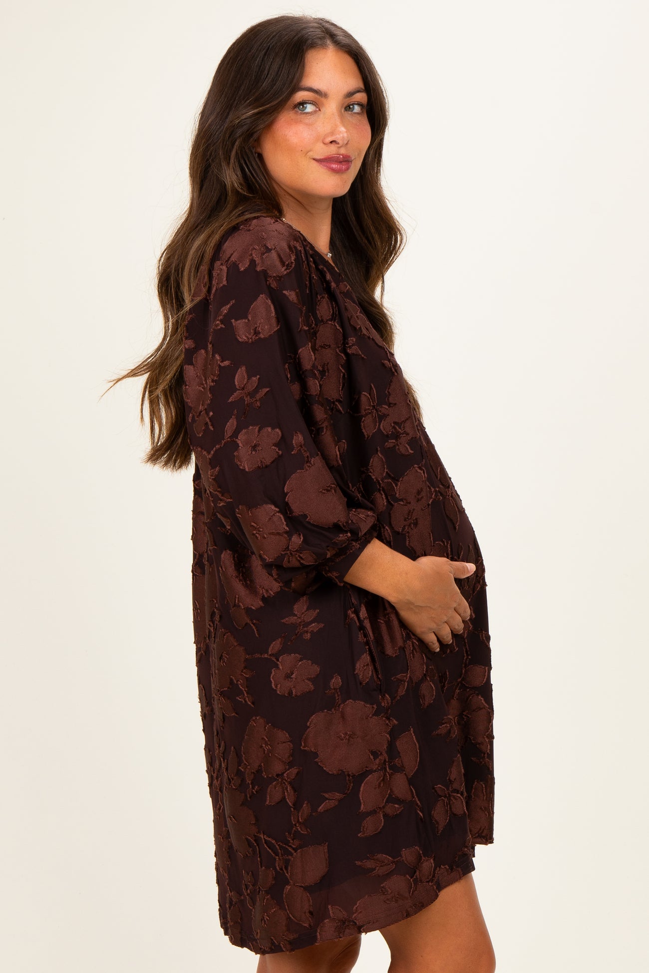 woman wearing a brown floral maternity dress with three-quarter sleeves and holding her baby bump