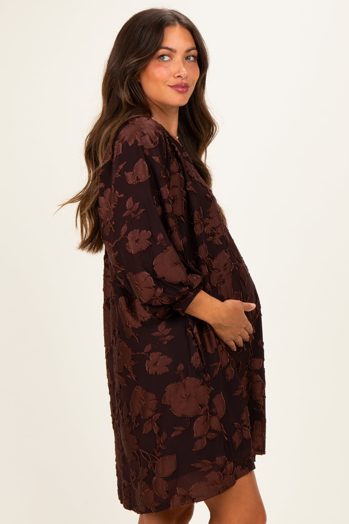 woman wearing a brown floral maternity dress with three-quarter sleeves and holding her baby bump
