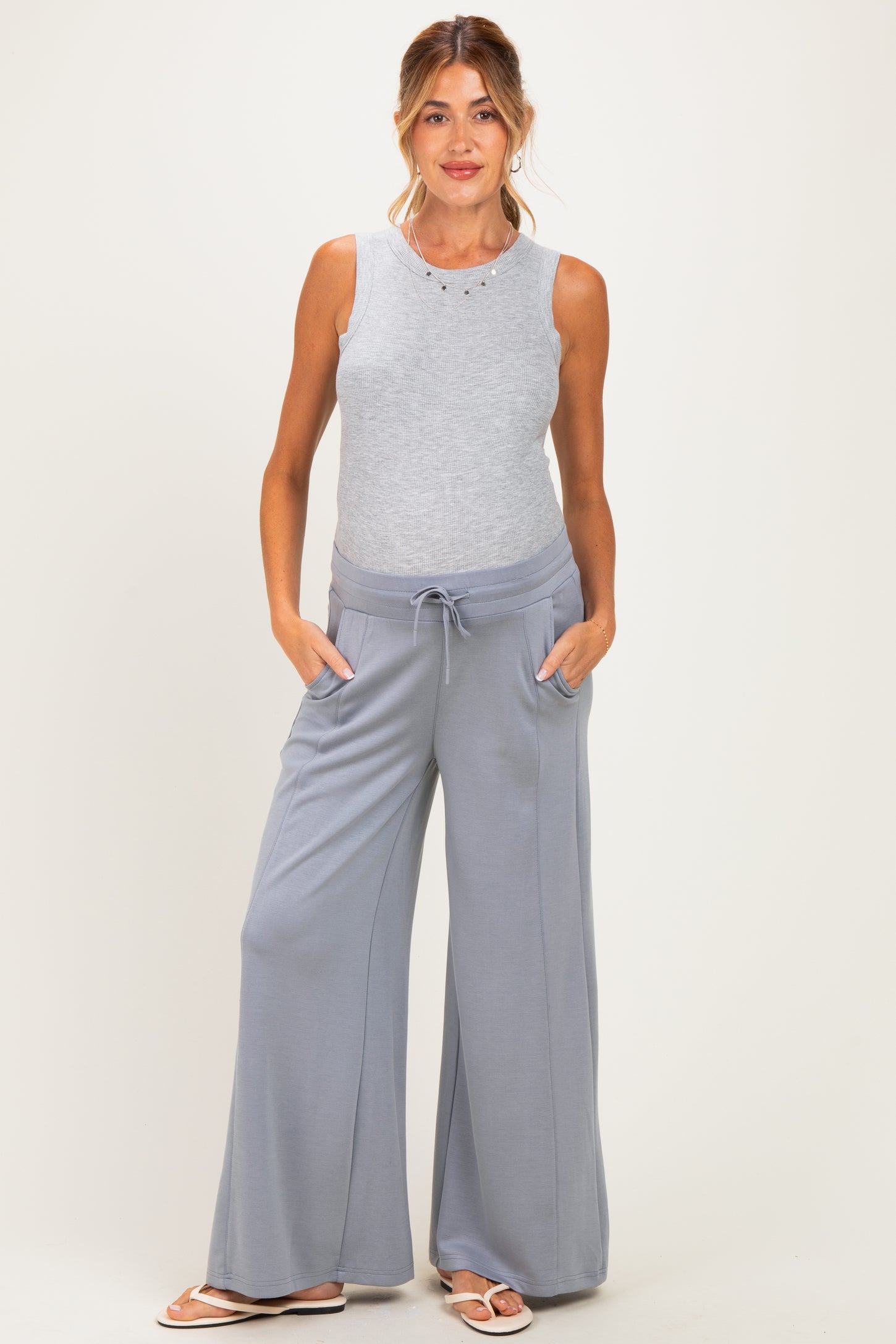 woman wearing a light gray sleeveless maternity top and wide-leg maternity pants with pockets, showing her baby bump
