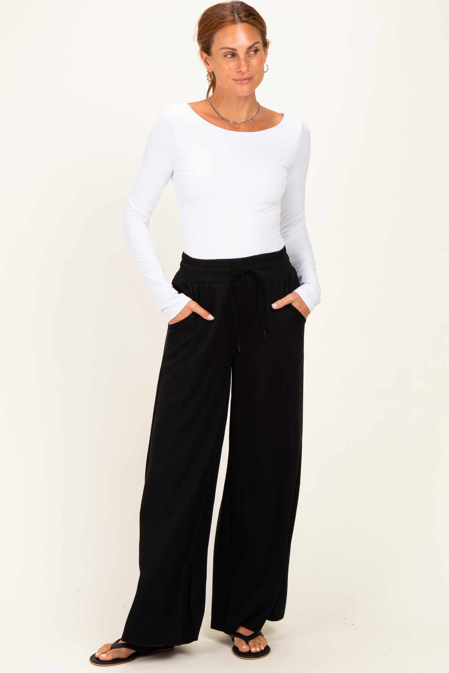 woman wearing a white long sleeve top and black wide leg pants with pockets, standing against a neutral background
