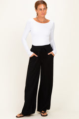woman wearing a white long sleeve top and black wide leg pants with pockets, standing against a neutral background