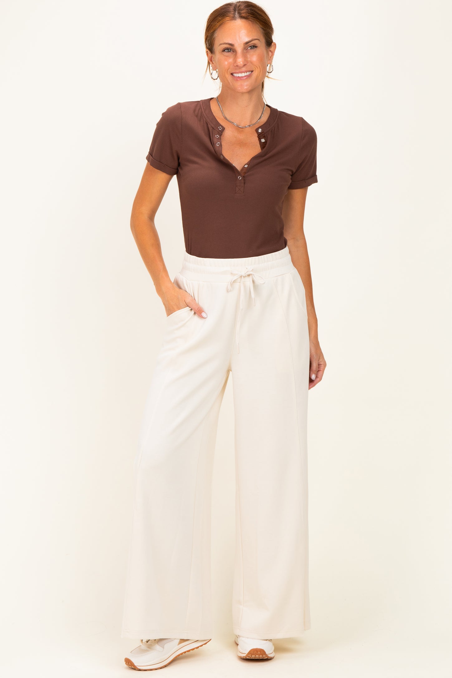 woman wearing a brown short sleeve henley top and white wide-leg pants with side pockets