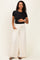 woman wearing a black short sleeve top and cream wide leg maternity pants, holding her baby bump
