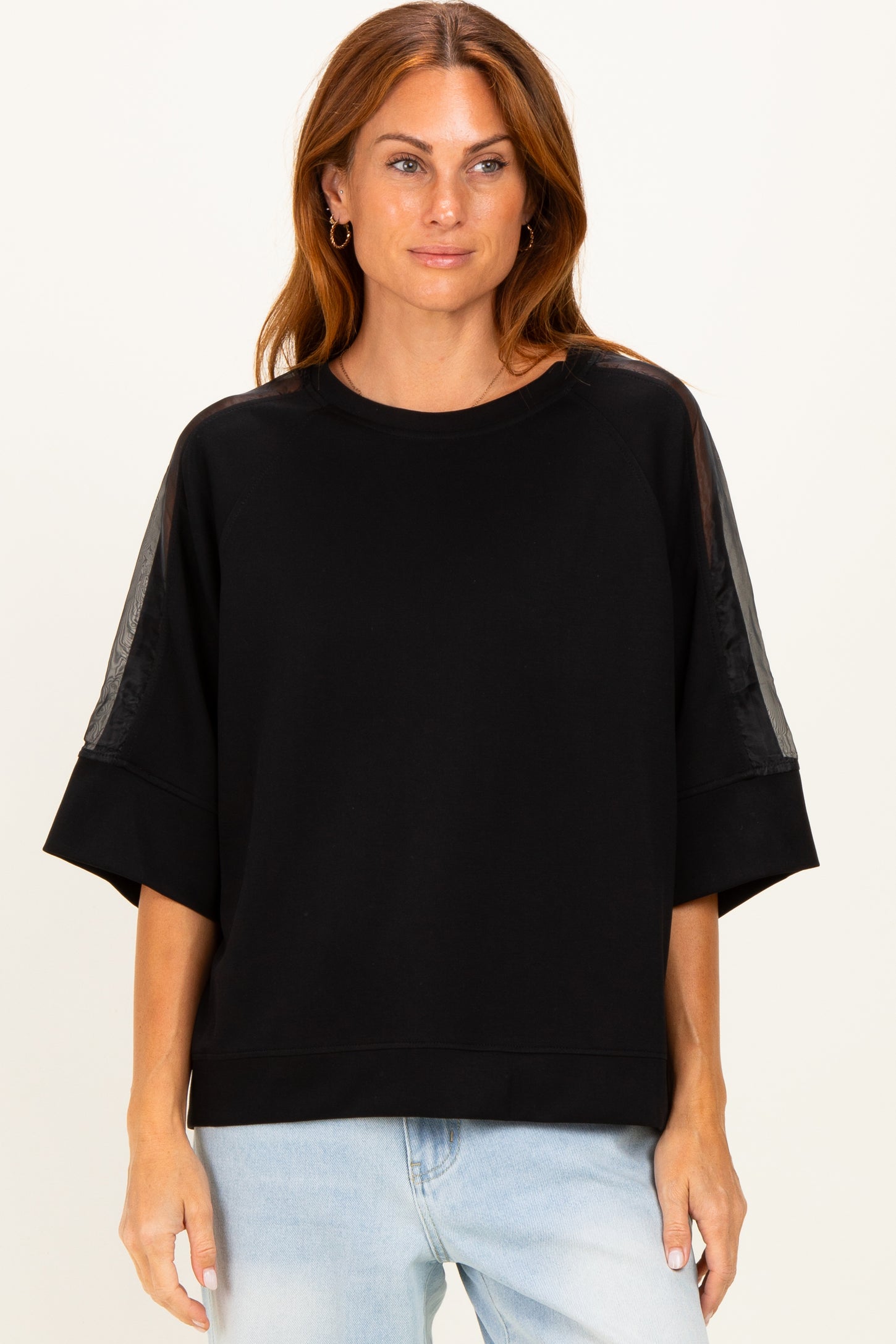 woman wearing a black oversized sweatshirt with sheer panels on the sleeves and a relaxed fit, styled with light blue jeans