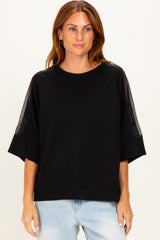 woman wearing a black oversized sweatshirt with sheer panels on the sleeves and a relaxed fit, styled with light blue jeans