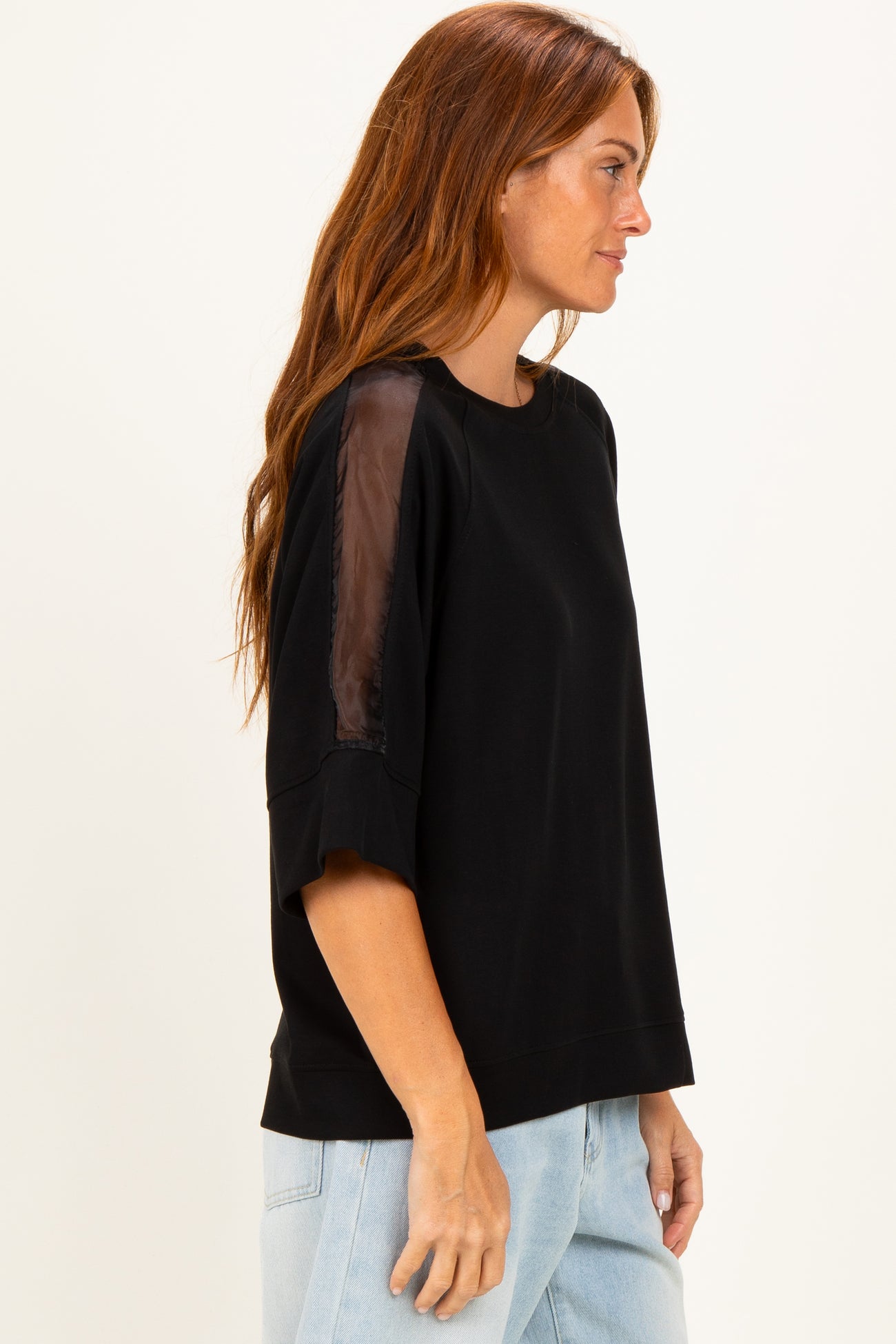woman wearing a black oversized sweatshirt with sheer sleeves and relaxed fit, styled with light wash jeans