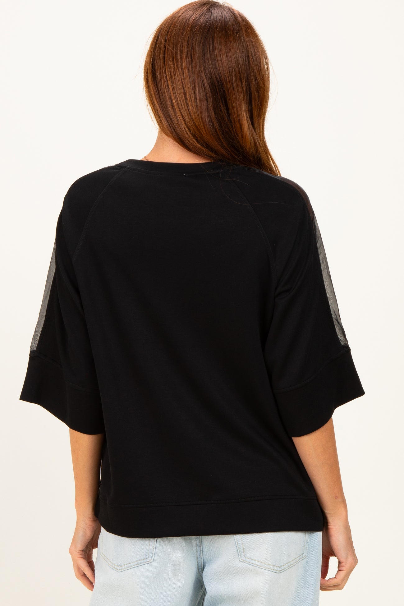 woman wearing a black oversized sweatshirt with mesh detail on the sleeves, view from the back