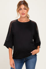 woman wearing a black maternity top with sheer sleeve details and a baby bump visible