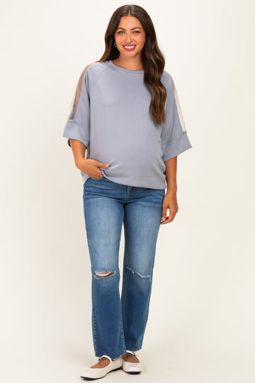 woman wearing a light blue maternity sweatshirt with sheer sleeves and pocket, paired with distressed jeans