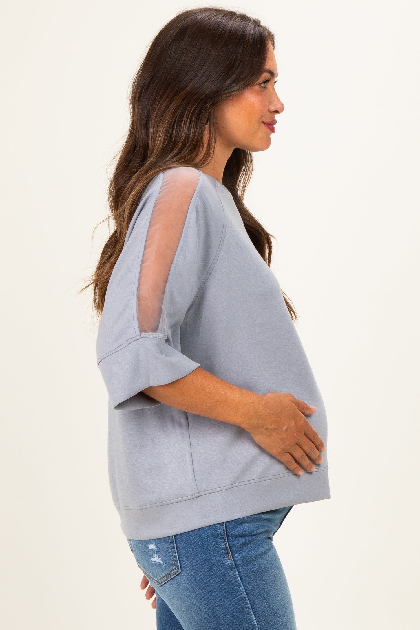 woman wearing a light gray maternity top with sheer sleeves and a visible baby bump
