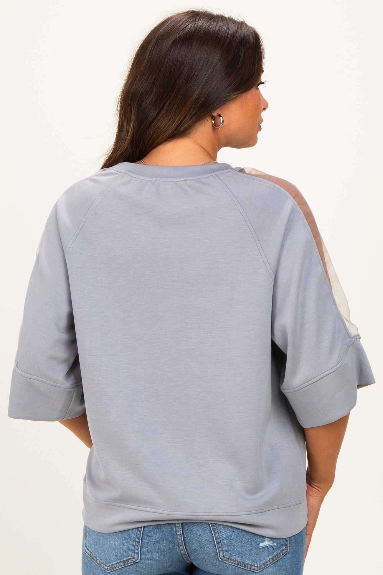 woman wearing a grey maternity sweatshirt with sheer panel details on the sleeves, seen from the back
