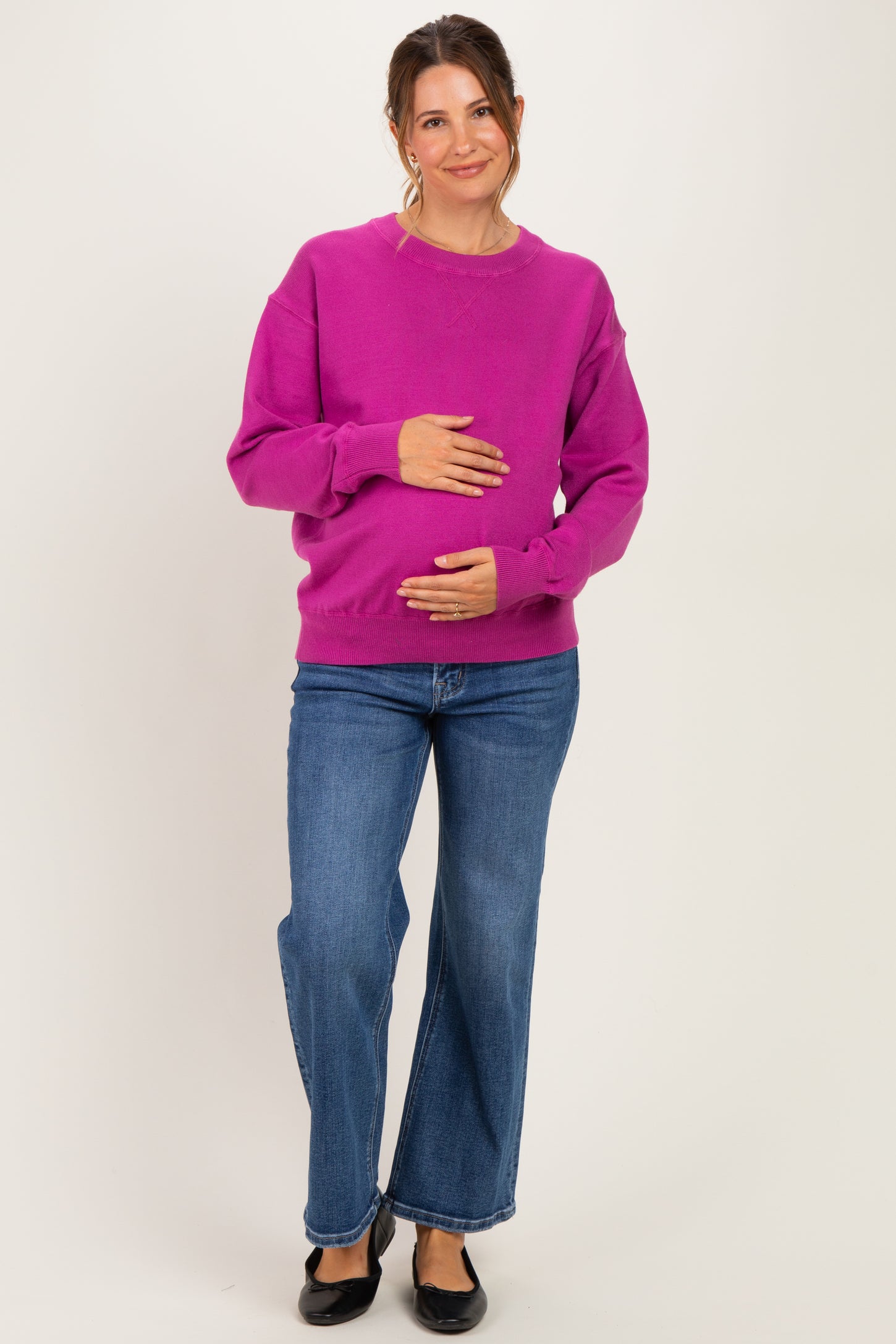 woman wearing a bright pink maternity sweater and holding her baby bump, paired with wide-leg jeans
