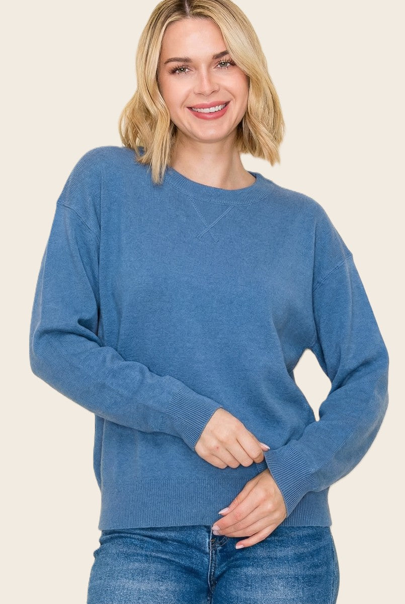 woman wearing a blue oversized sweater with long sleeves and a round neckline, smiling at the camera