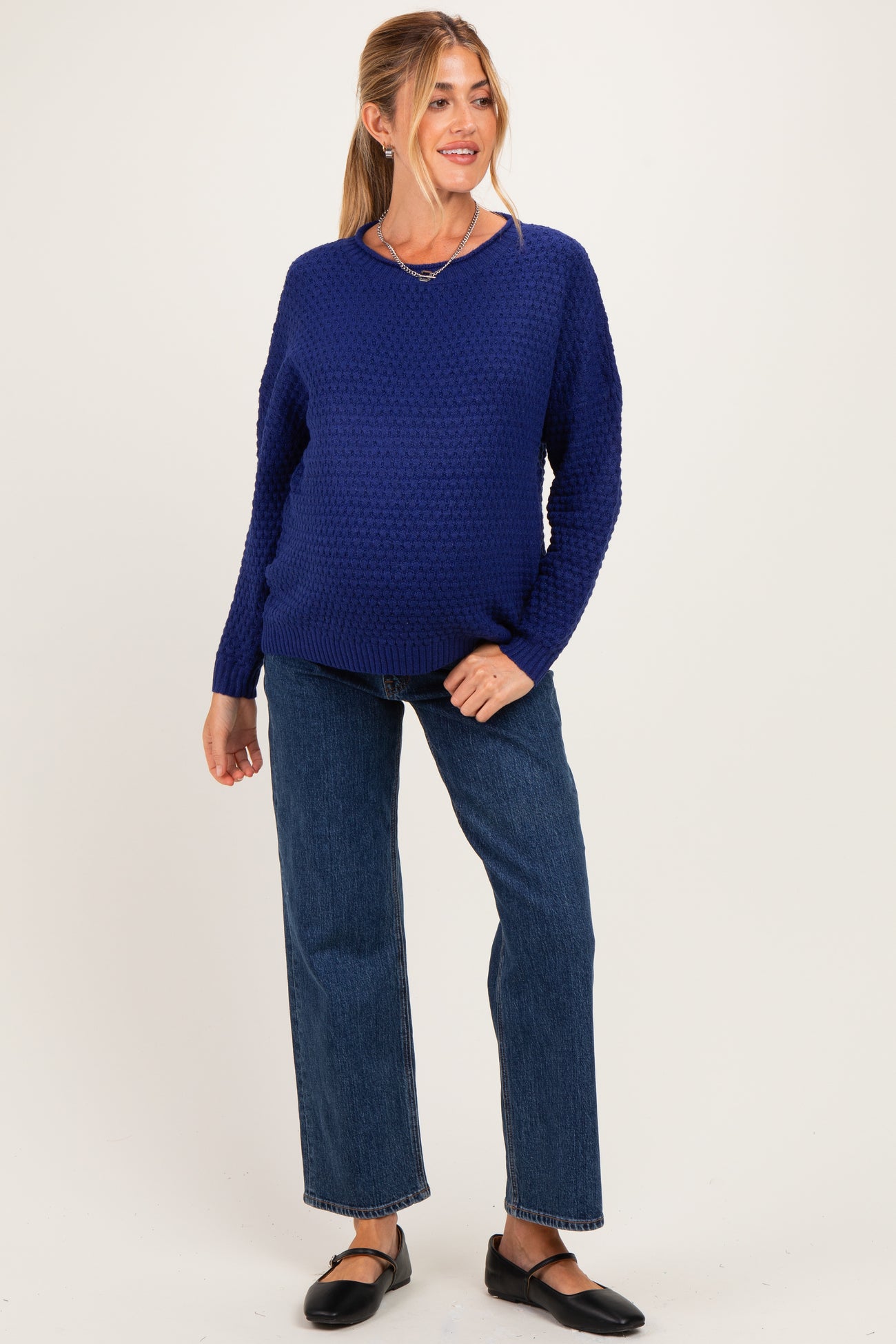 woman wearing a navy blue knitted maternity sweater and blue straight leg jeans, showing her baby bump