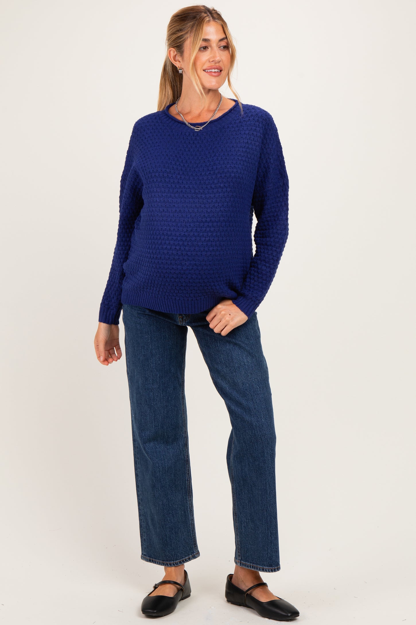 woman wearing a navy blue knitted maternity sweater and blue straight leg jeans, showing her baby bump