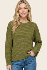 woman wearing an olive green textured knit sweater with long sleeves and a relaxed fit, paired with blue jeans