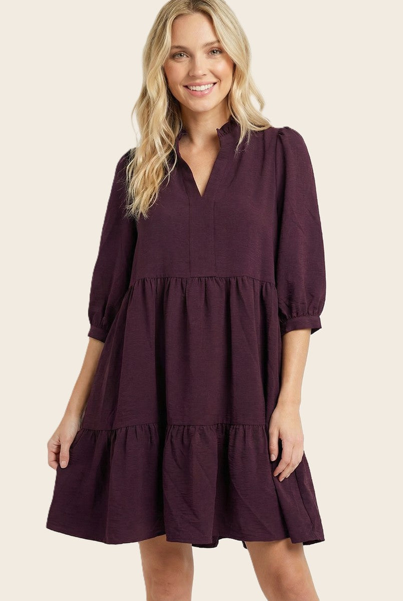 woman wearing a burgundy loose fit tiered dress with three-quarter sleeves and a v-neckline