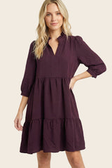 woman wearing a deep purple short sleeve tiered dress with a v-neck and ruffle details