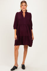 woman wearing a dark burgundy maternity dress with puff sleeves and a tiered hem, styled with black mules